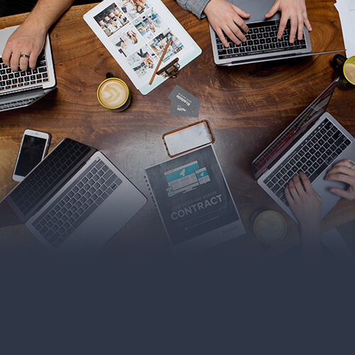 Multiple laptops with hands typing and books on a table